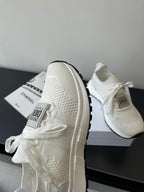 White Dior sneakers viewed from the side, showing lace ties and thick sole