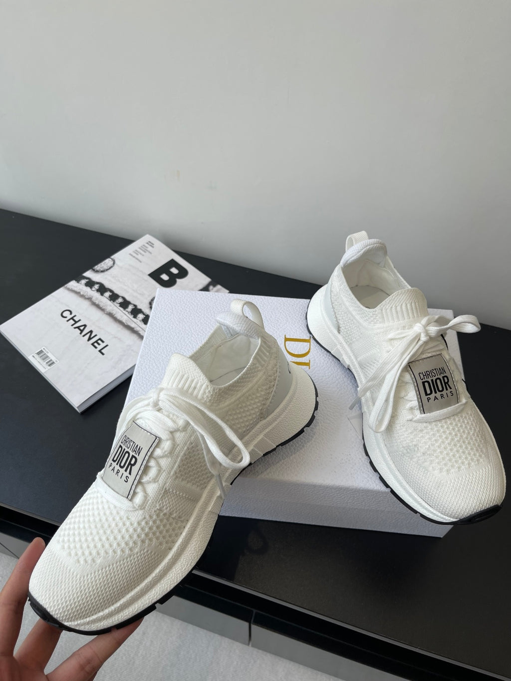Pair of white Dior knit sneakers on display, with lace ties and cushioned sole