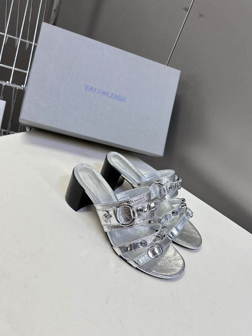 Silver slide sandals with layered buckles and black block heel, side view