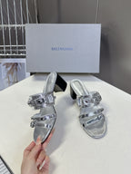 Silver slide sandals with buckle straps and black block heel, held up