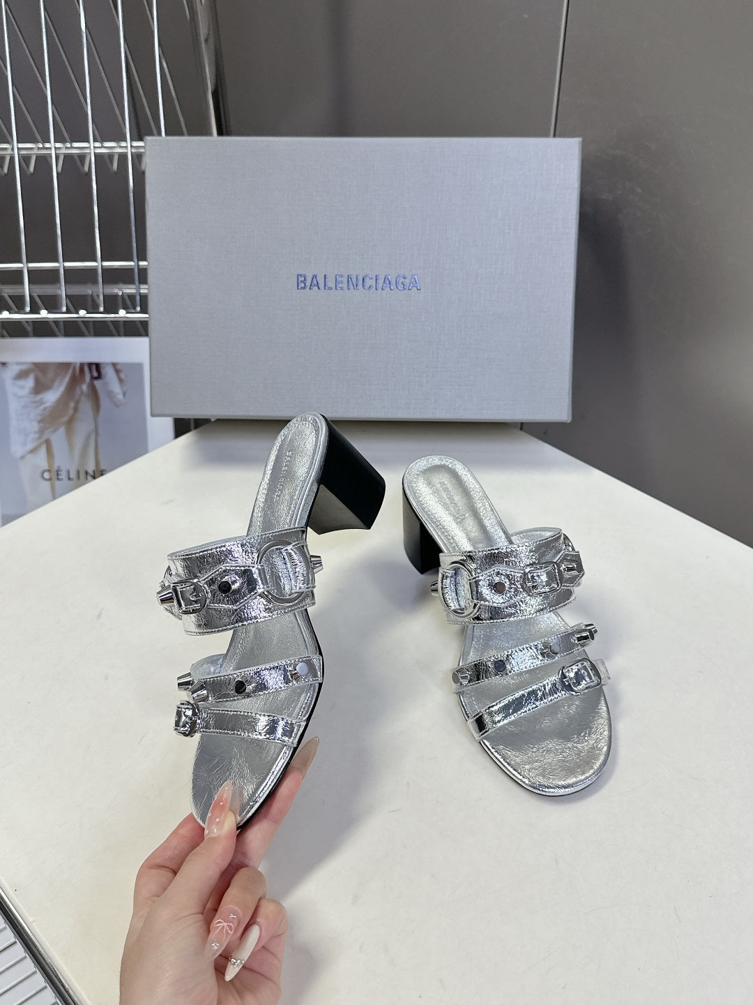Silver slide sandals with buckle straps and black block heel, held up