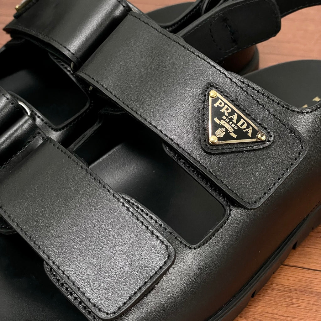 Prada unisex black sandal strap close-up with triangular logo patch and stitched details