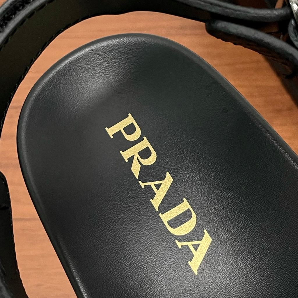 Prada sandal footbed close-up with gold logo lettering on black leather