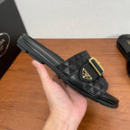 Black Prada slide sandal on hand, geometric strap and gold buckle; flat sole.