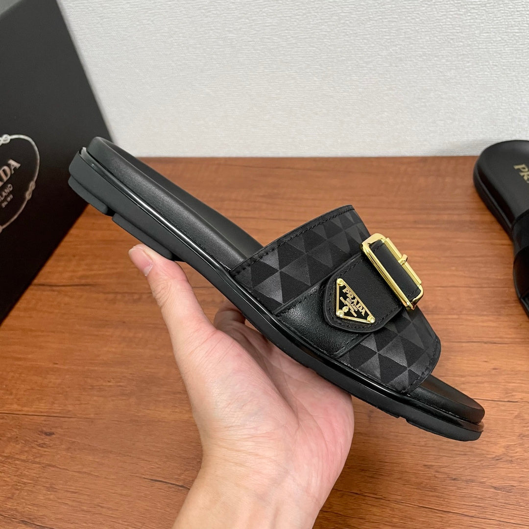 Black Prada slide sandal on hand, geometric strap and gold buckle; flat sole.