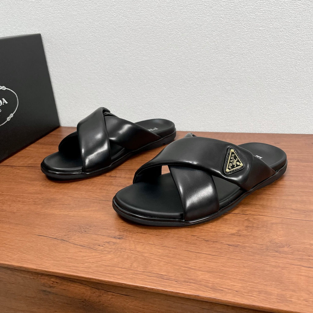 Black leather slide sandals with cross straps and gold logo plaque on upper