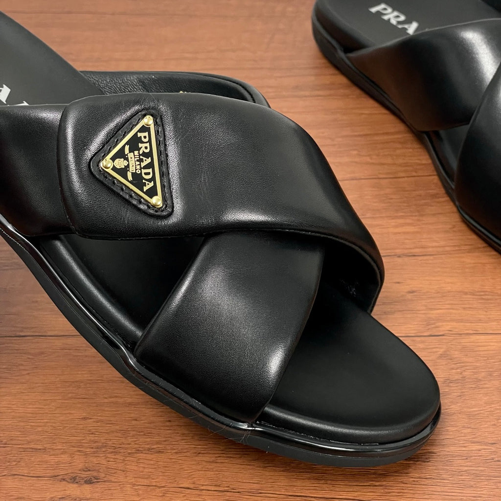 Close-up of black slide sandal upper with gold Prada logo plaque