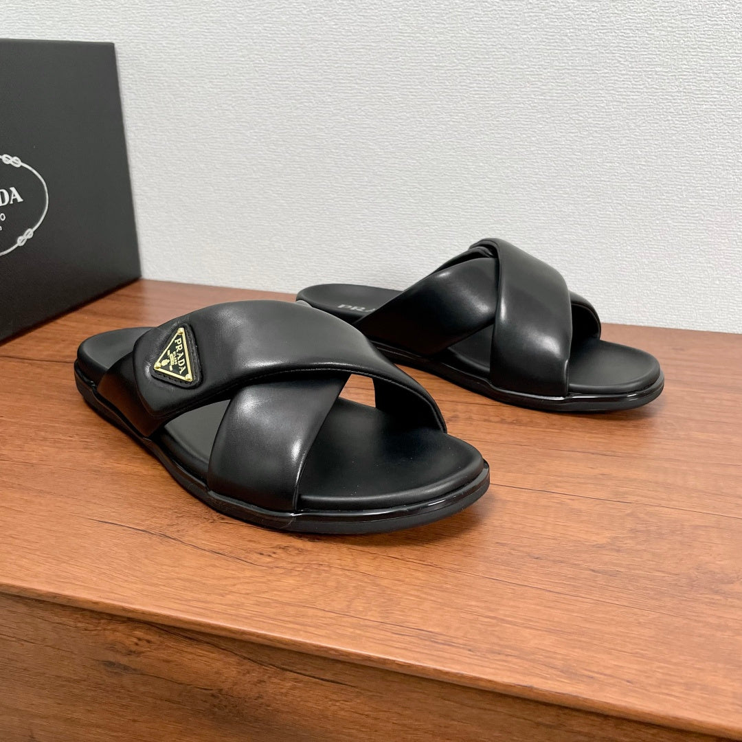 Black leather slide sandals with crisscross straps and gold logo patch on top