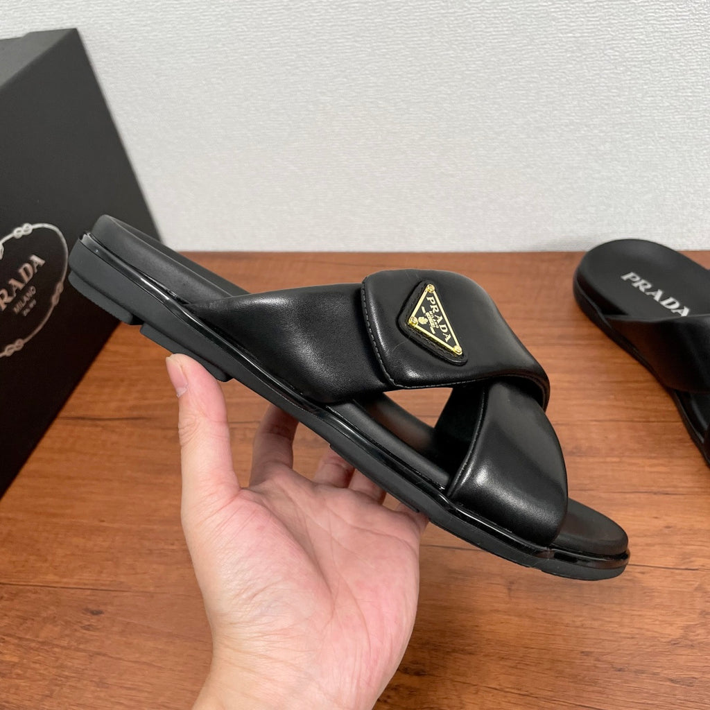 Black leather slide sandal held in hand, wide strap with gold logo patch