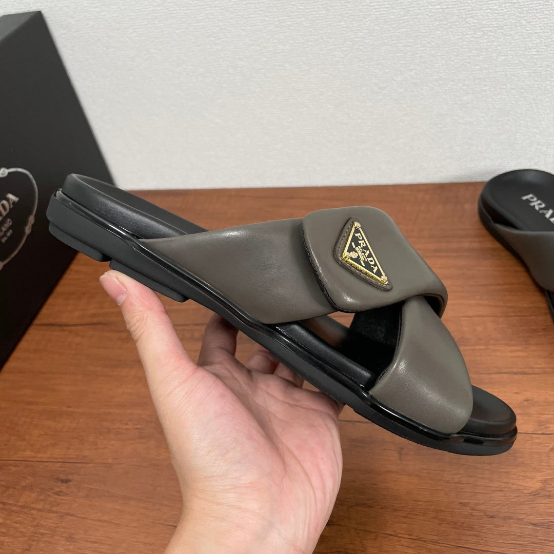 Gray Prada slide sandal held in hand, gold logo patch and black sole