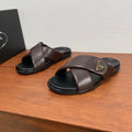 Brown leather slide sandals with black soles and gold logo plaque on upper