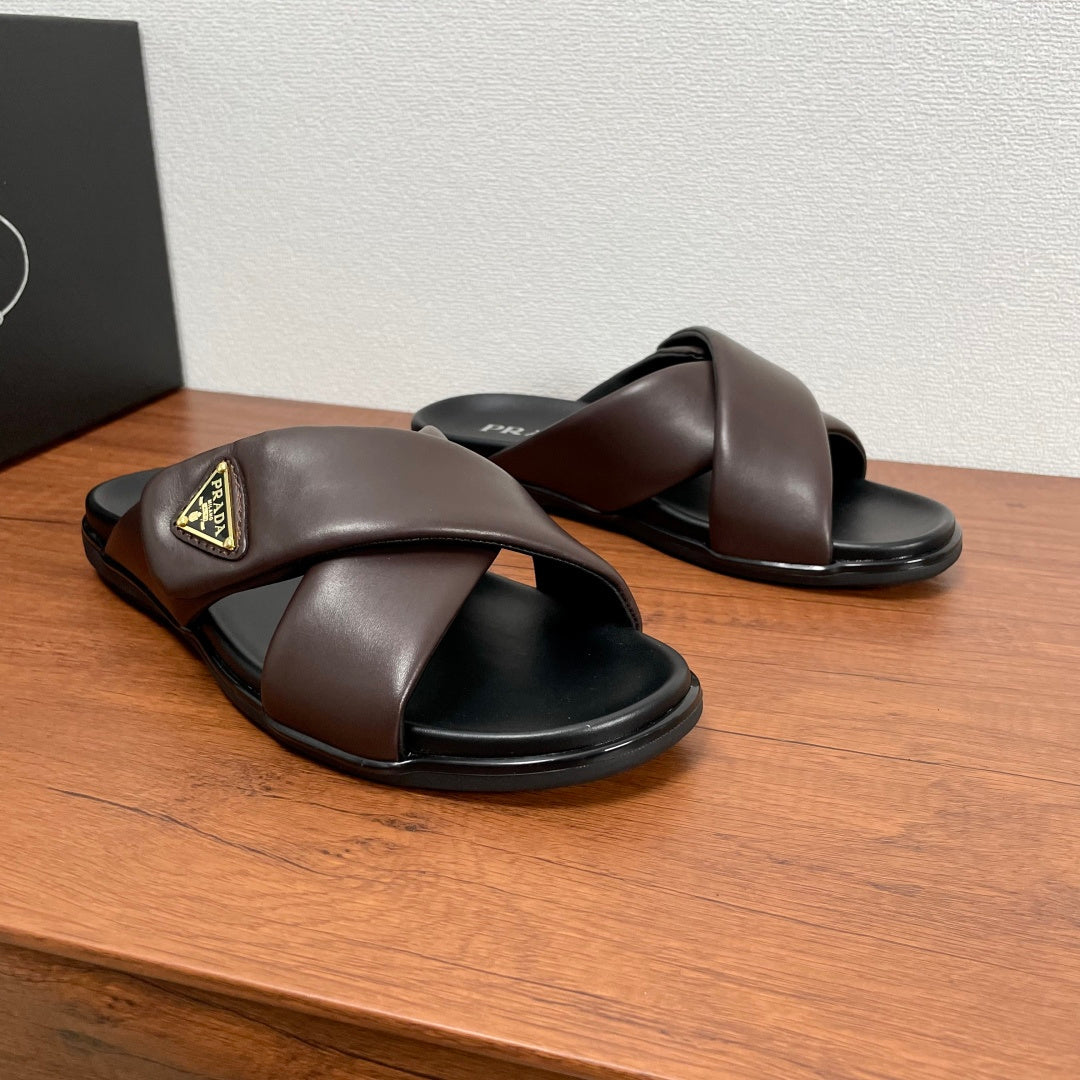 Dark brown slide sandals with X-style straps, black footbeds, and gold logo patch