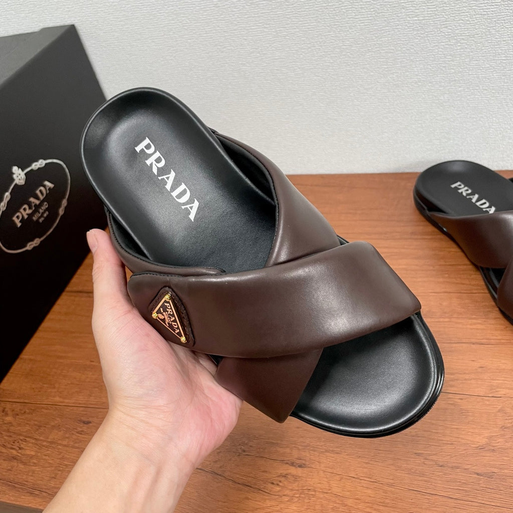 Dark brown slide sandal with PRADA logo on black footbed, held by hand