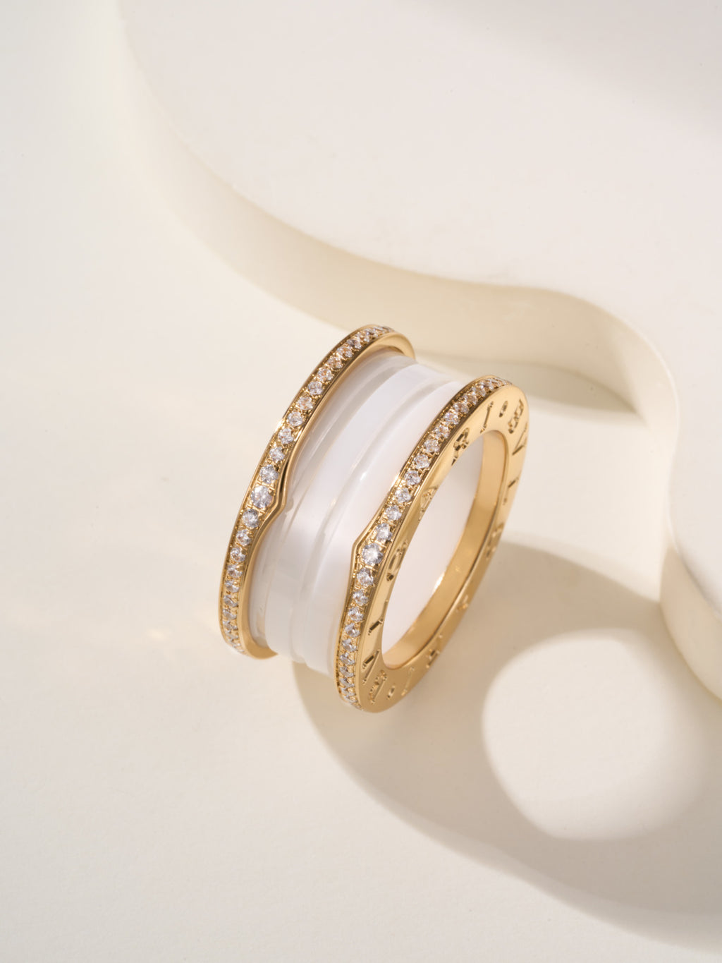 Gold-tone ring with white enamel band and pavé sparkle trim, side view
