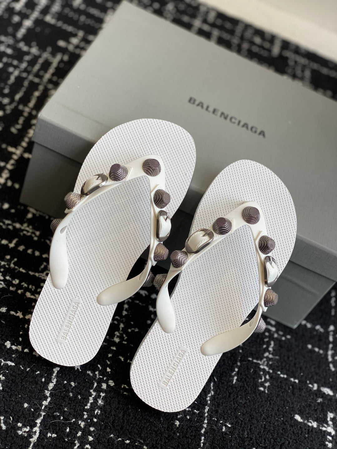 Pair of white thong sandals with circular stud straps and metal buckle