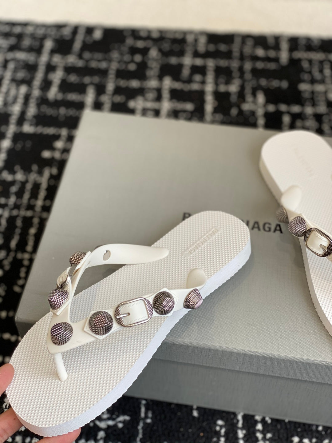 White thong sandals with studded strap and metal buckle, close-up