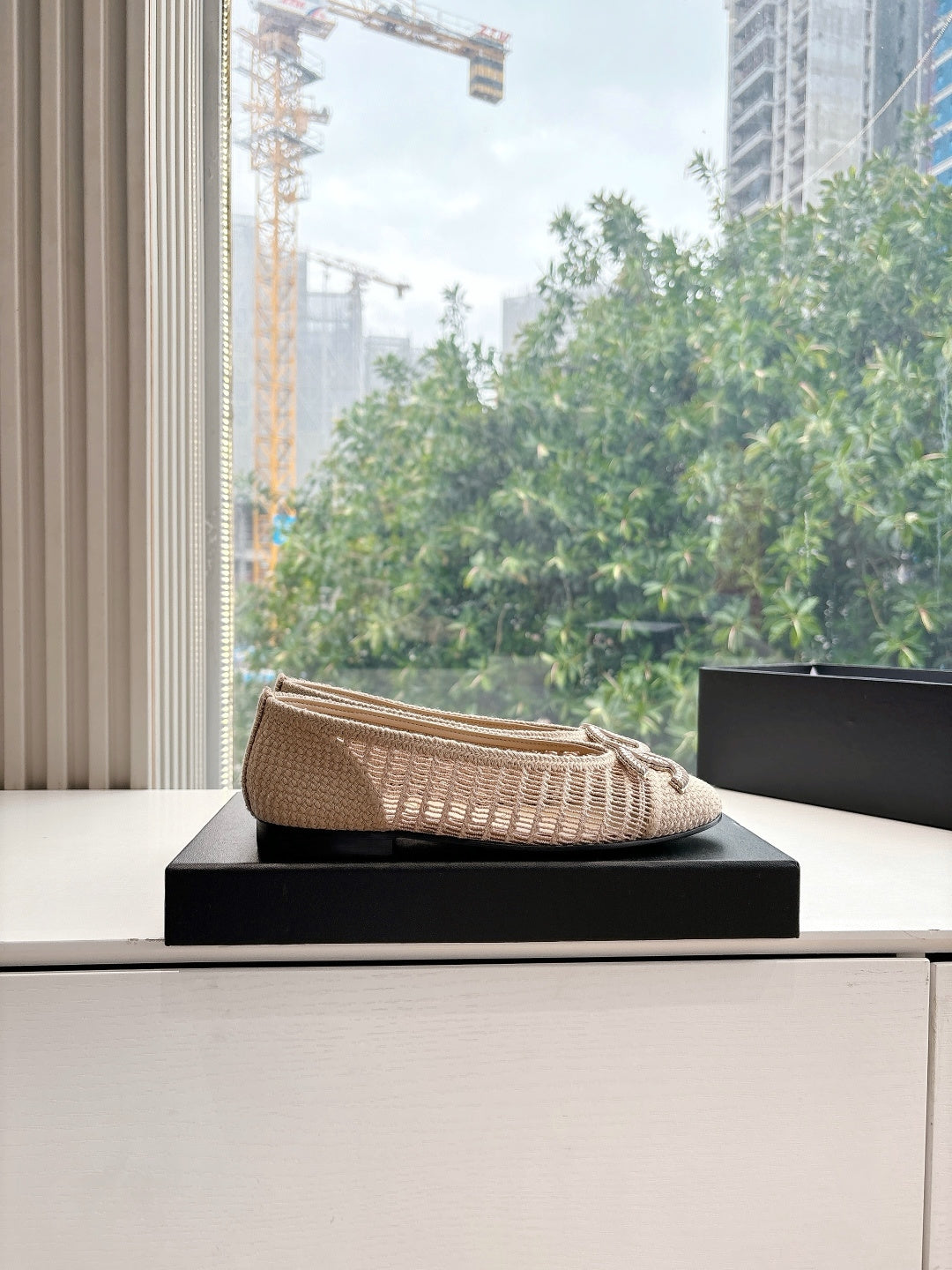 Beige woven ballet flats with braided bow detail, angled view on box.