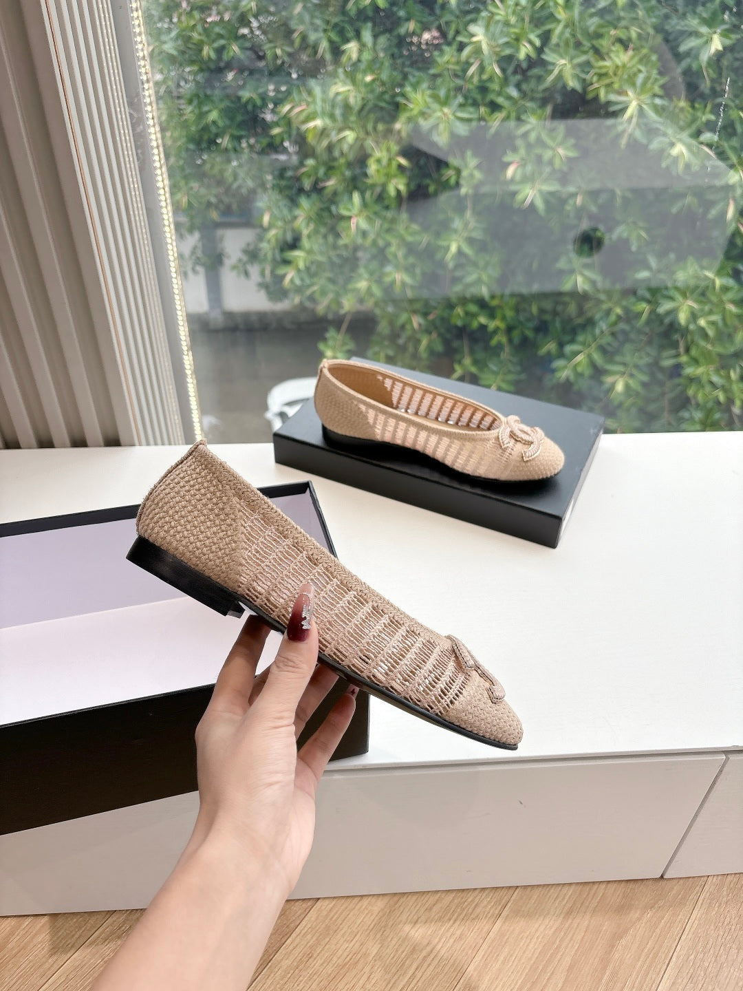 Beige woven ballet flat with braided bow detail held in hand, front view.