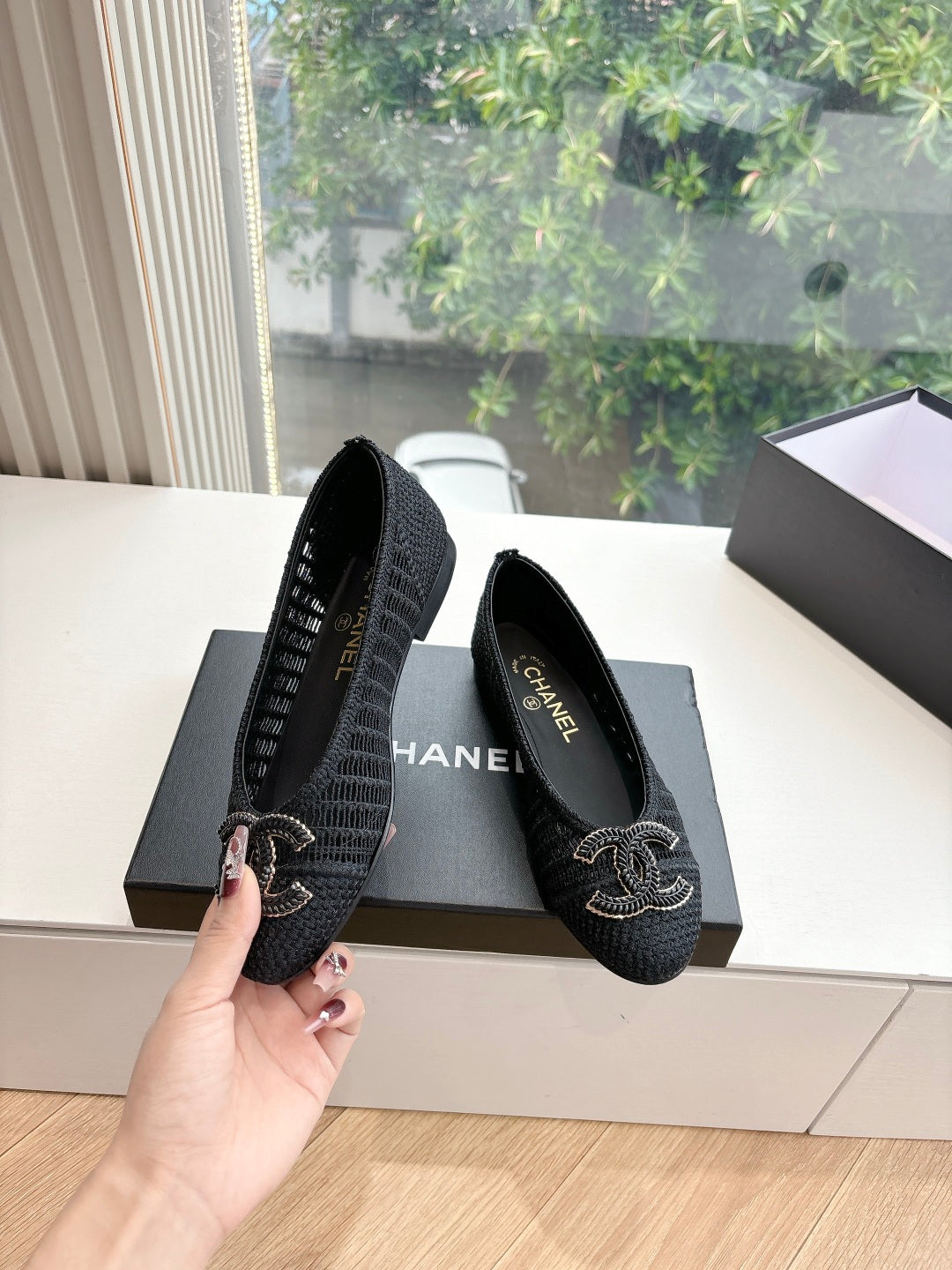 Black Chanel knit slip-on flats held in hand; CC logo embroidery on toe