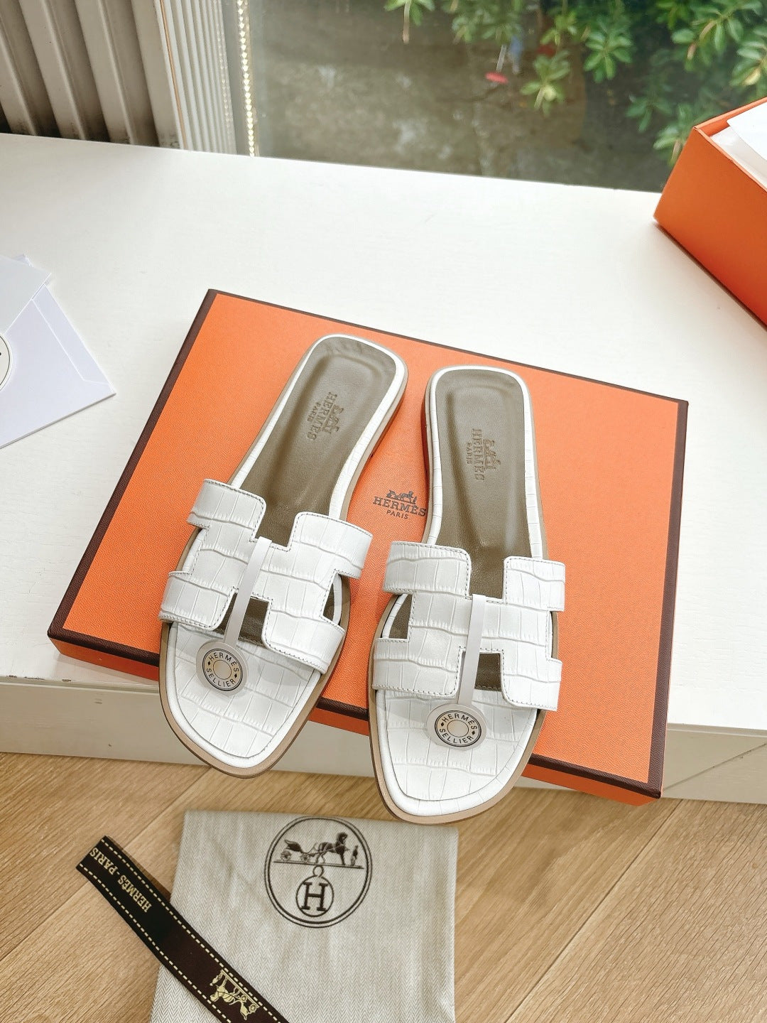 Hermes ladies' slide sandals paired in box with white straps and round logo emblem