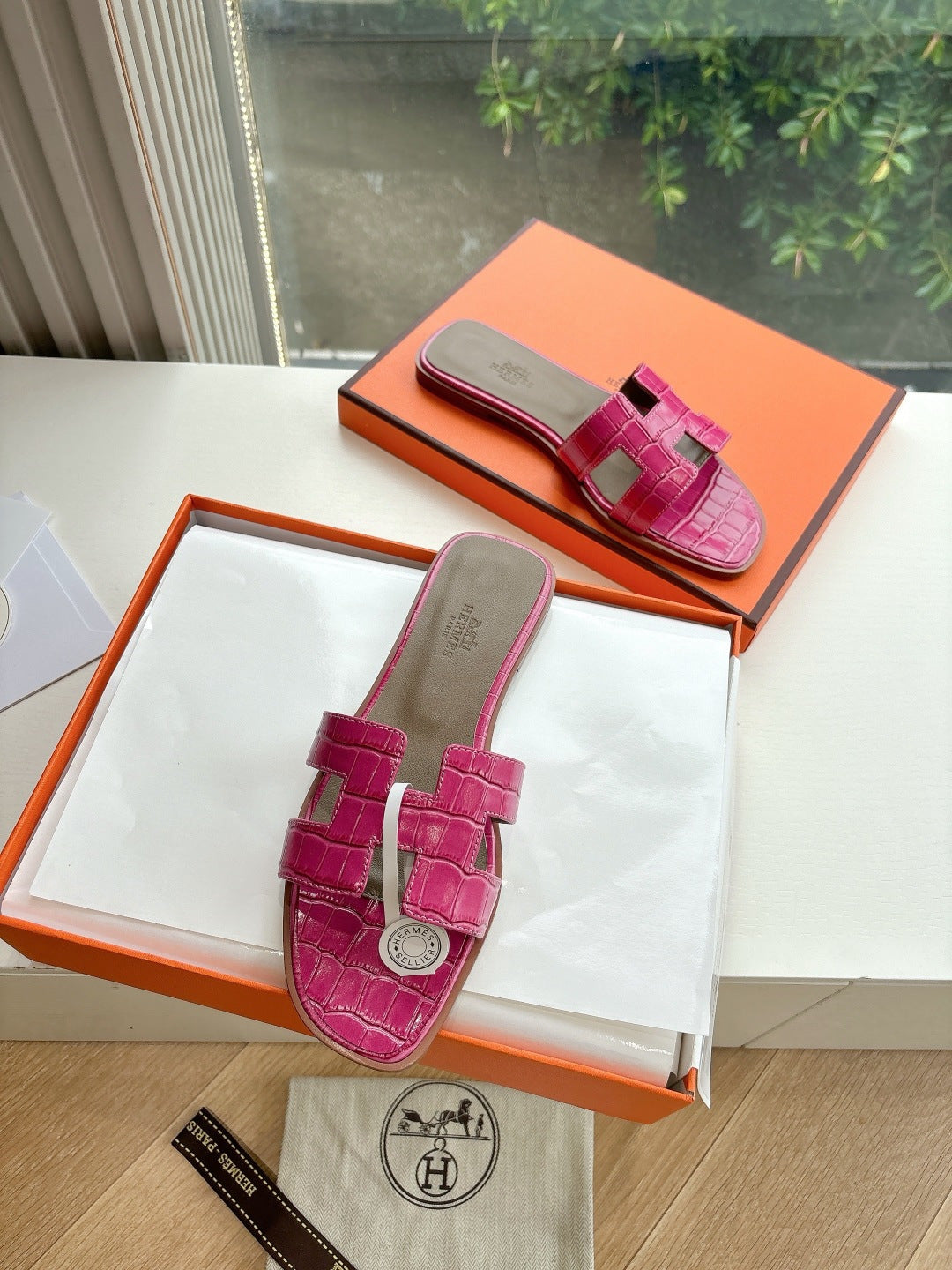 Hermes pink croc-pattern slide sandals on white box, front view