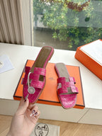 Hermes pink croc-pattern slide sandals held near orange box, side view