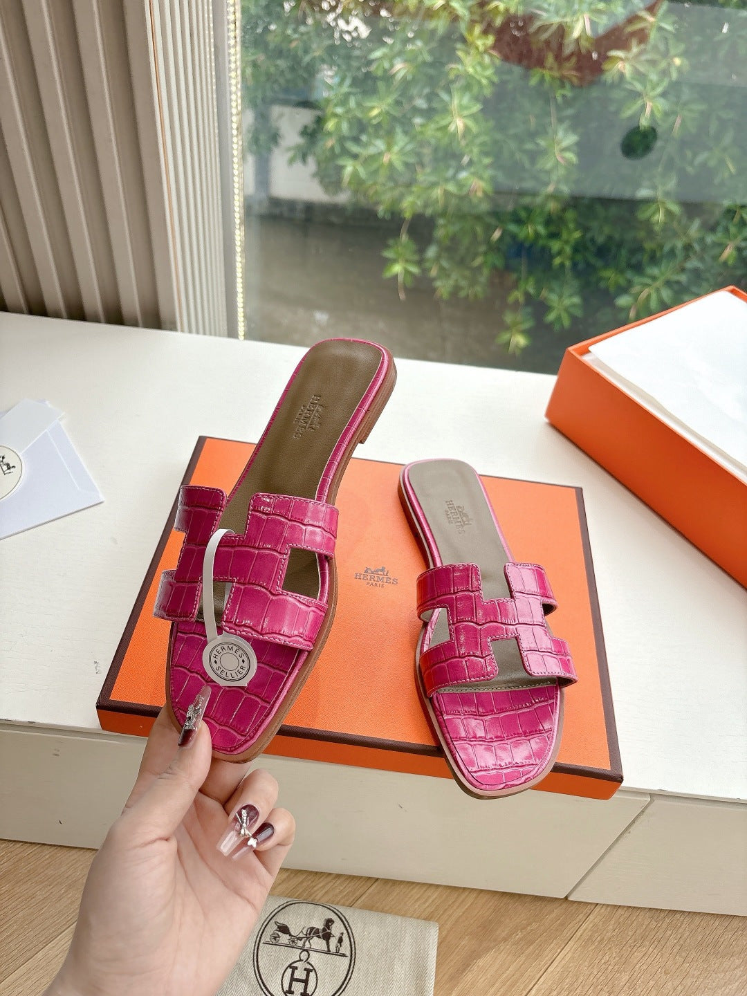 Hermes pink croc-pattern slide sandals held near orange box, side view