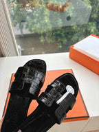 Black slide sandals with textured strap and round logo medallion on upper