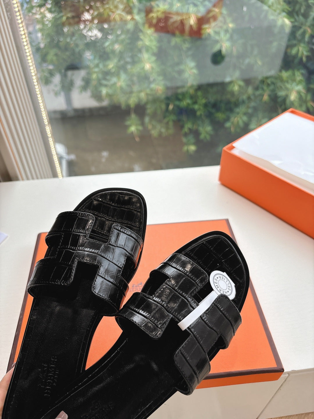 Black slide sandals with textured strap and round logo medallion on upper