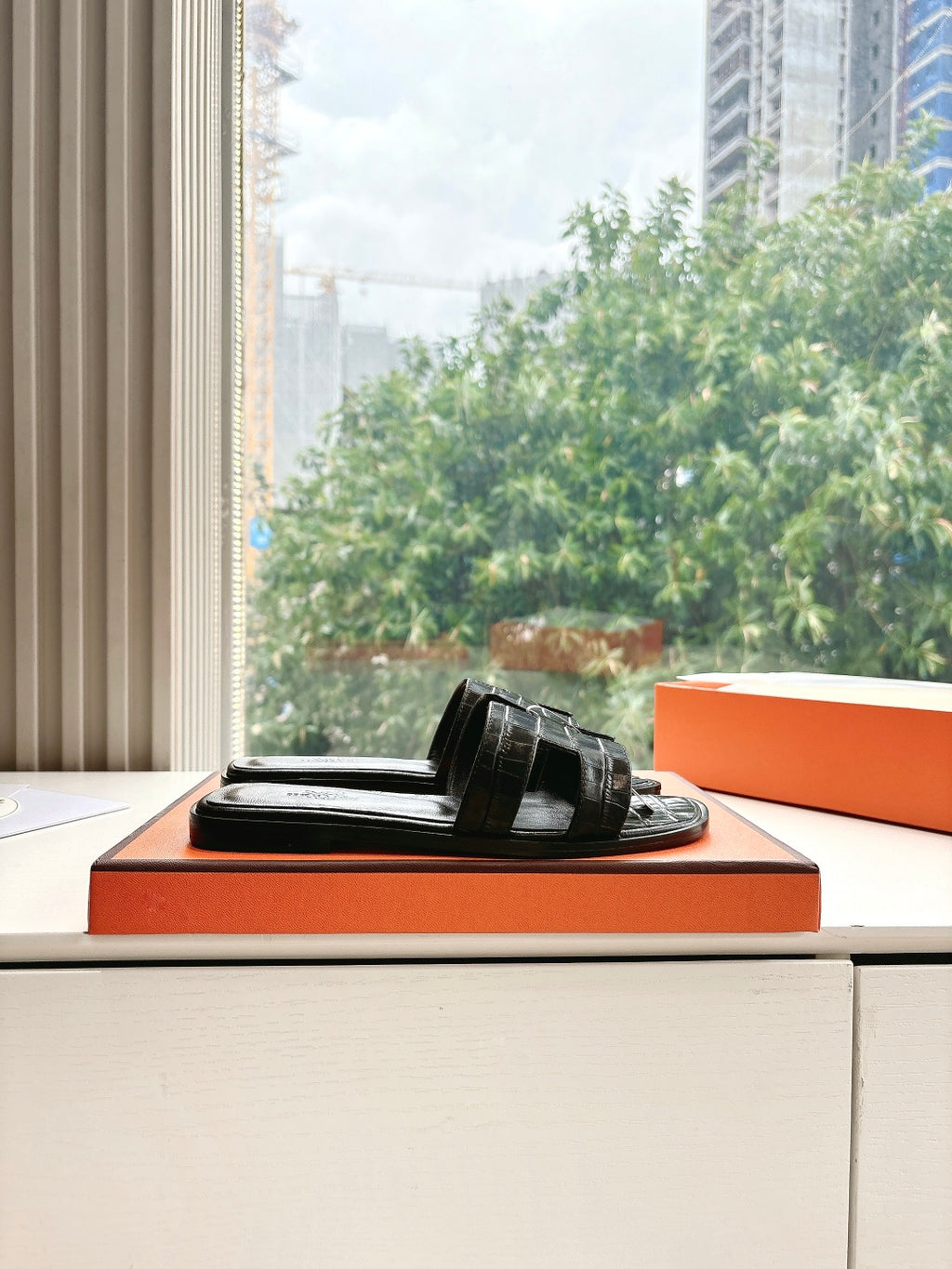Black leather slide sandal with buckle strap, resting on orange display box
