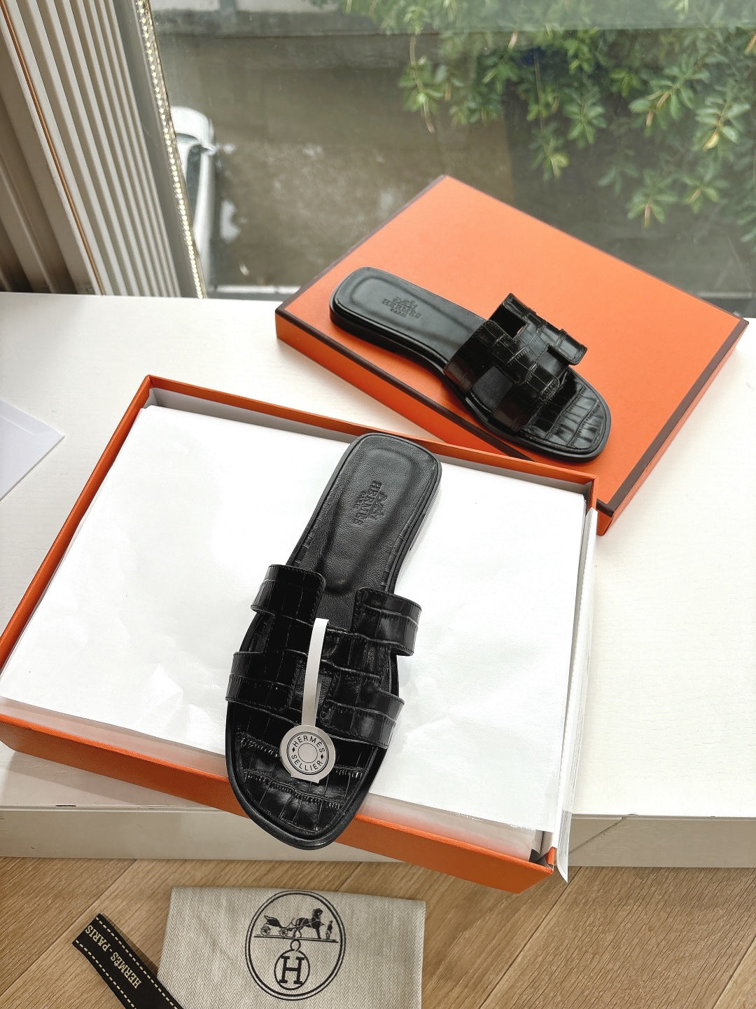 Black slide sandals with adjustable buckle strap and embossed sole logo on box