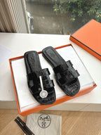 Black leather slide sandals with buckle straps and embossed logo, shown in gift box