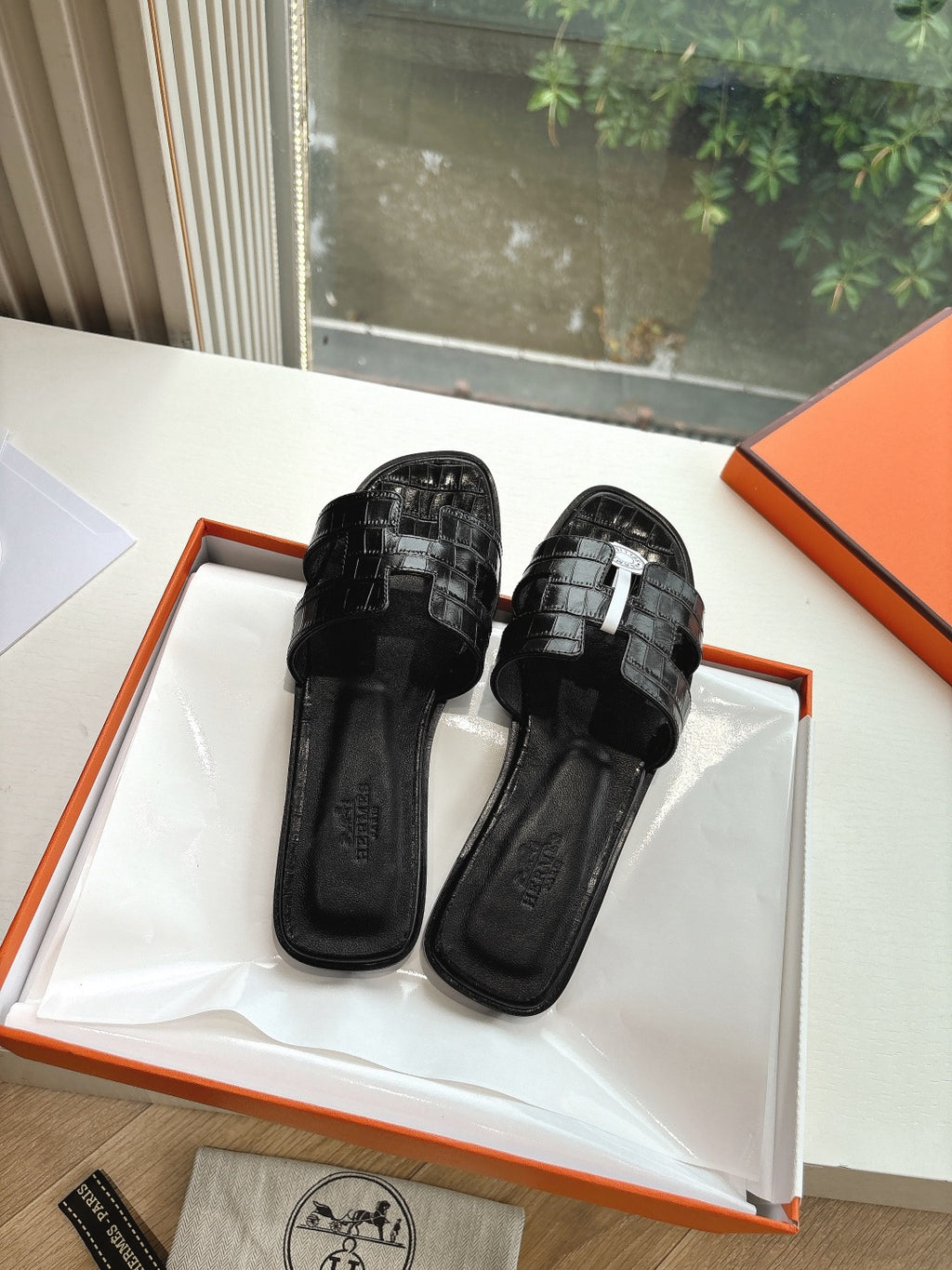 Black slide sandals with textured strap panels and round logo medallion on box