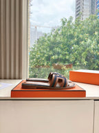 Hermes ladies mule sandals on display, brown leather slide with dark and white geometric strap
