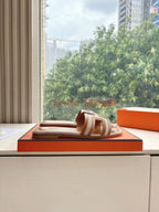 Single tan-and-brown leather slide sandal on orange shoebox lid