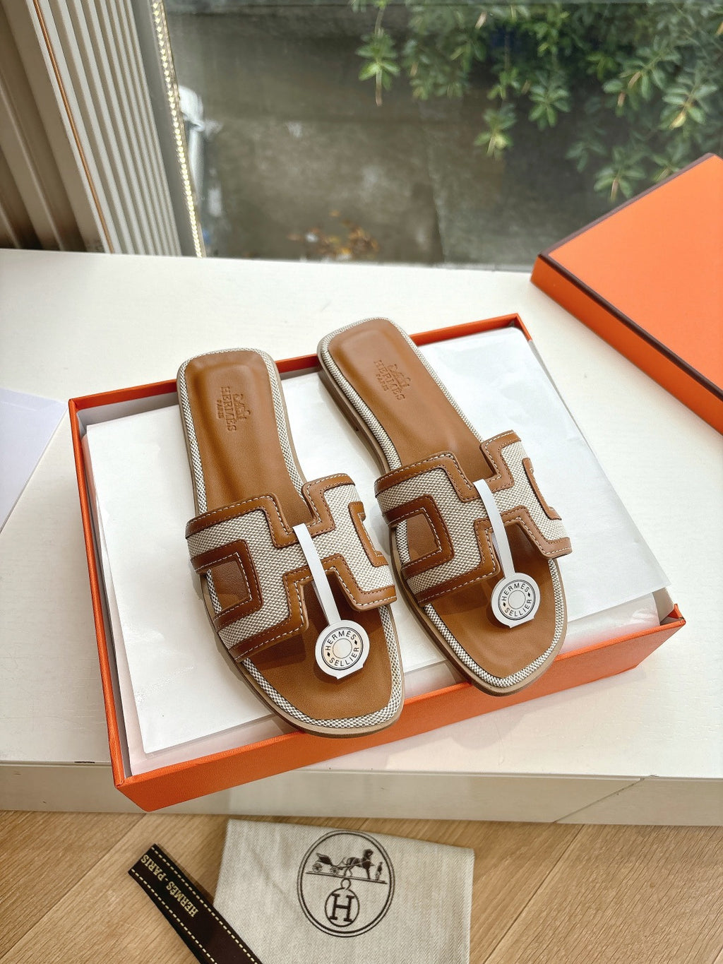 Tan-and-brown leather slide sandals with geometric strap and round logo emblem