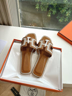 Pair of tan-and-brown leather slide sandals with H-style geometric straps and emblem