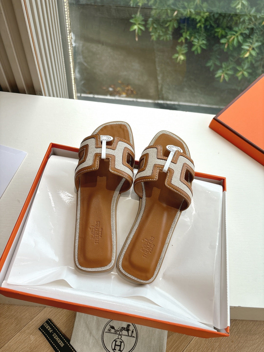 Pair of tan-and-brown leather slide sandals with H-style geometric straps and emblem