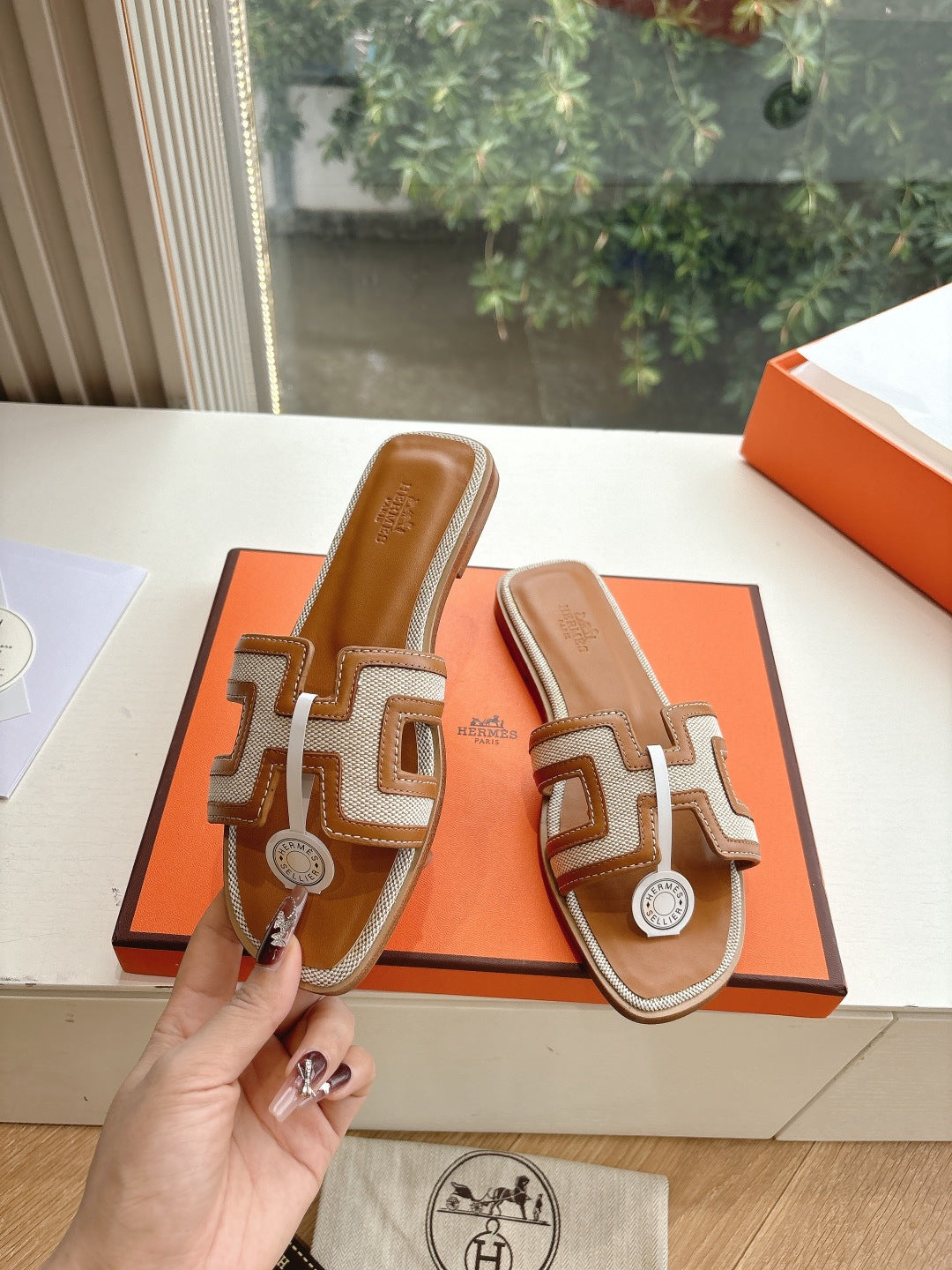 Tan-and-brown leather slide sandals held up, geometric straps with round emblem