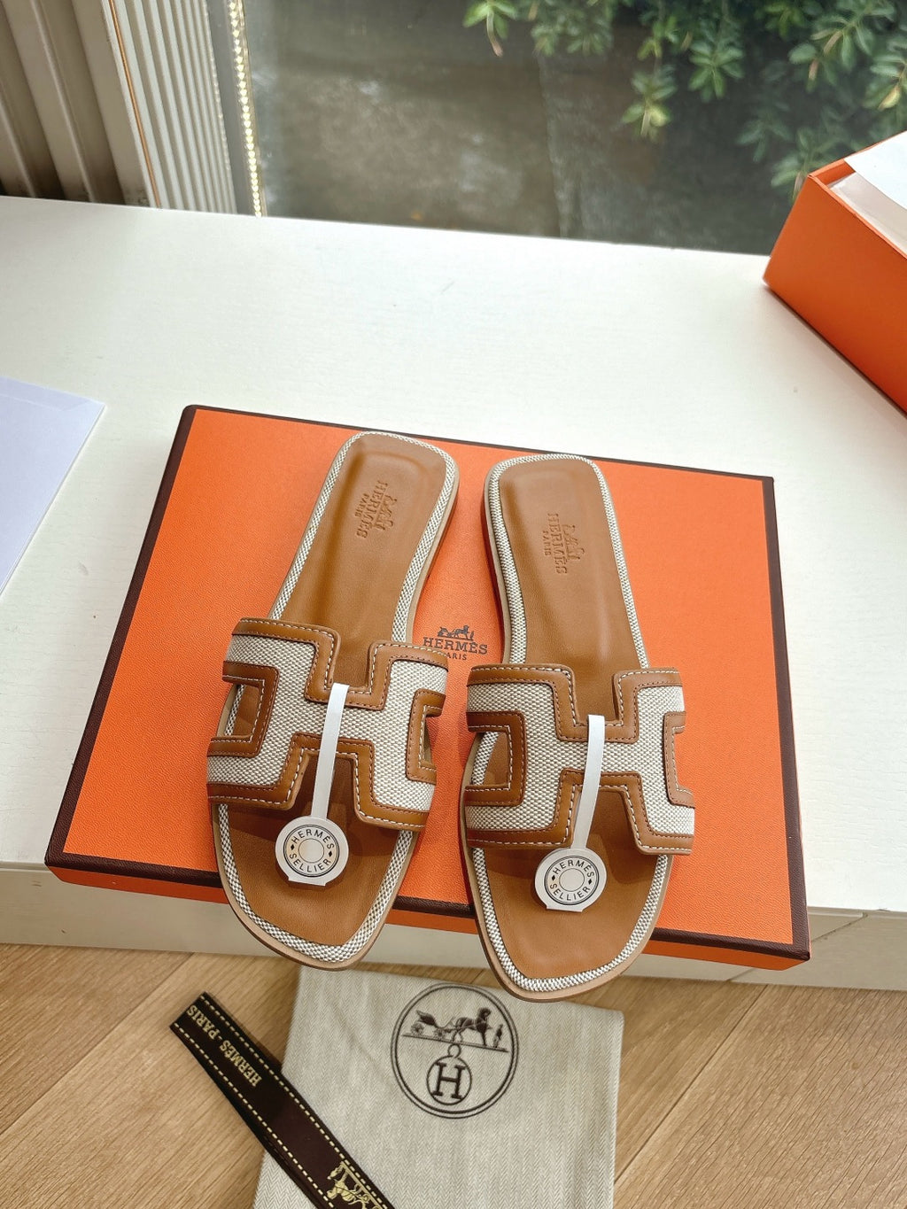Tan-and-brown leather slide sandals with geometric straps and round logo emblem
