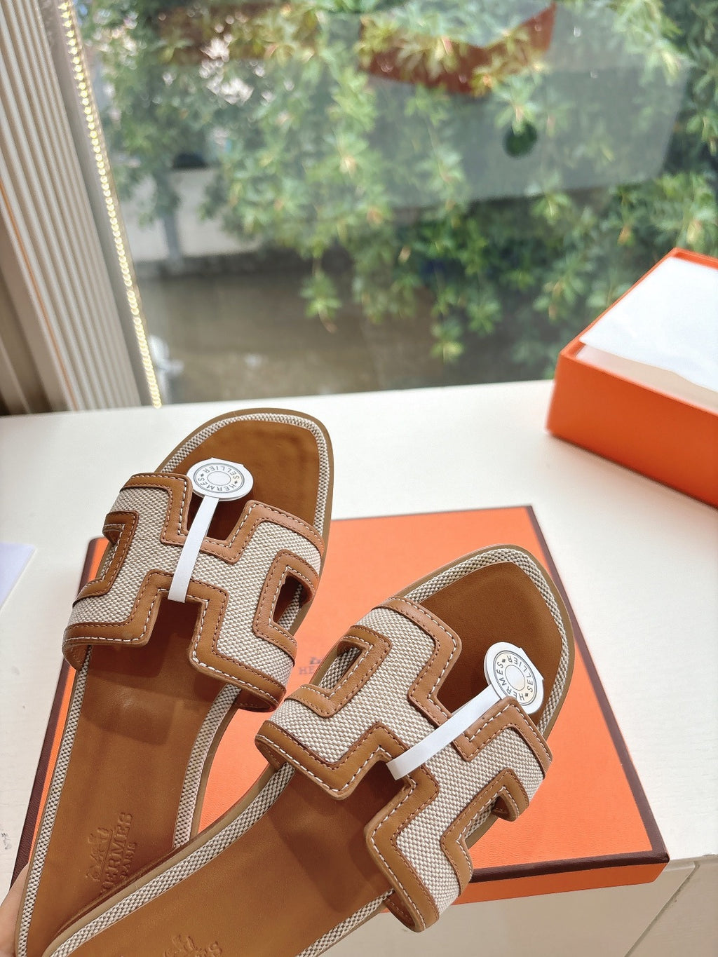 Tan-and-brown leather slide sandals close view of geometric straps and round emblem