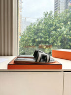 Hermes slide sandals on orange box top, black with white H-style straps.