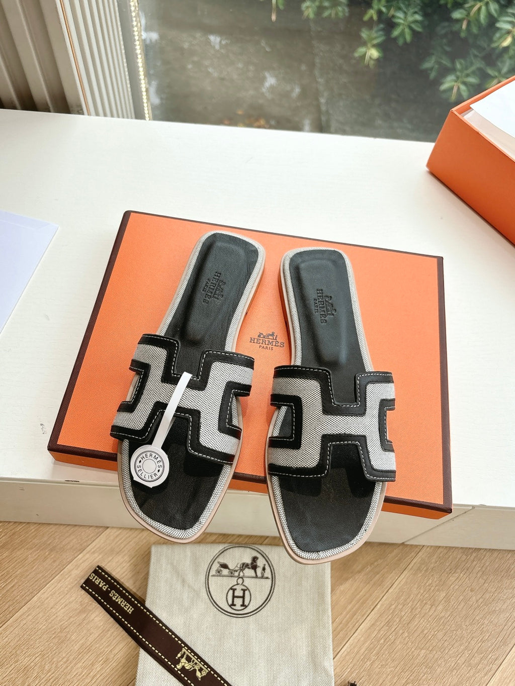 Hermes slide sandals with black uppers and white H-style straps, in orange box.