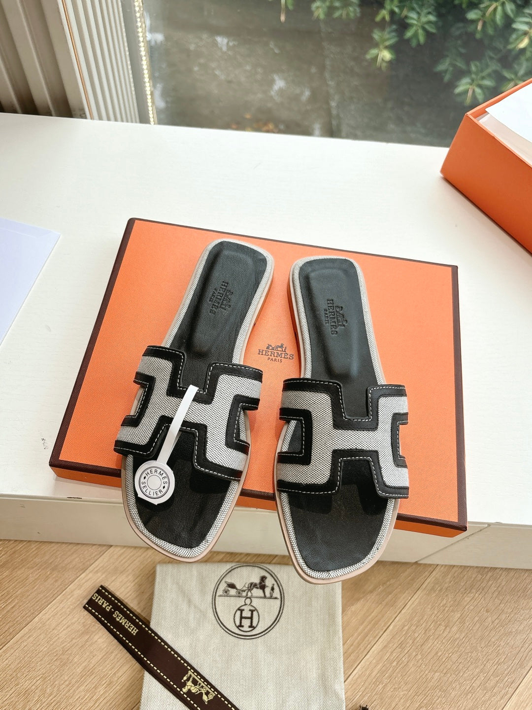 Hermes slide sandals with black uppers and white H-style straps, in orange box.