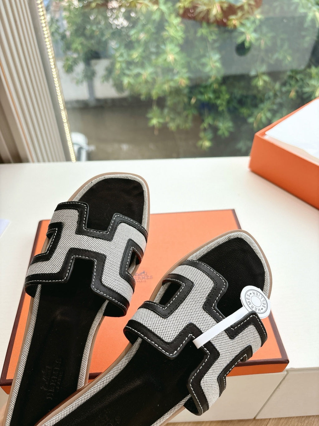 Hermes slide sandals black with white H-style straps, resting on open orange box.