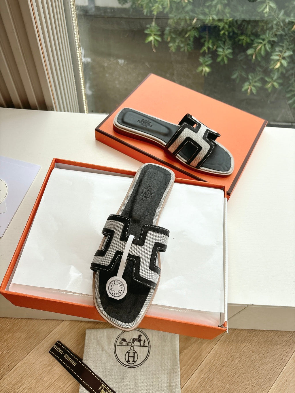 Hermes slide sandals, black with white H-style straps, in orange shoebox.