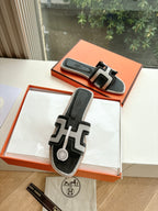 Hermes slide sandals, black with white H-style straps, in orange shoebox.