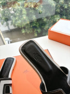 Black Hermes slide sandal with textured insole and H-style strap, close-up.