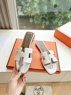 Women’s slide sandals by Hermes, white leather slides with buckle straps shown in hand
