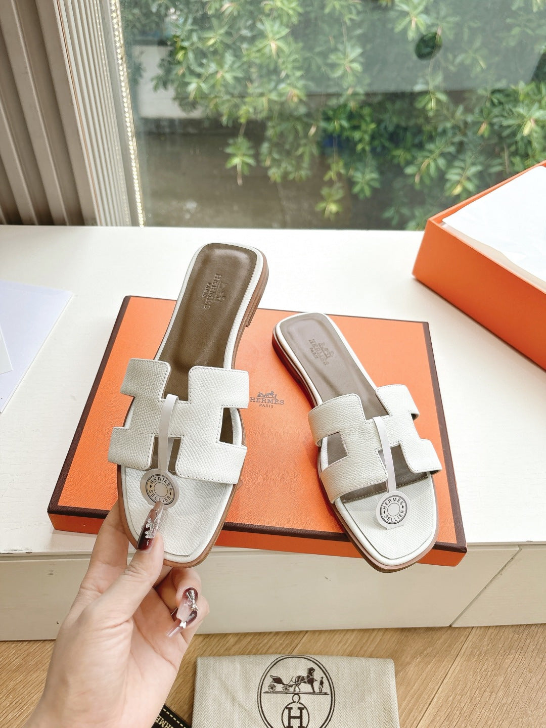 Women’s slide sandals by Hermes, white leather slides with buckle straps shown in hand